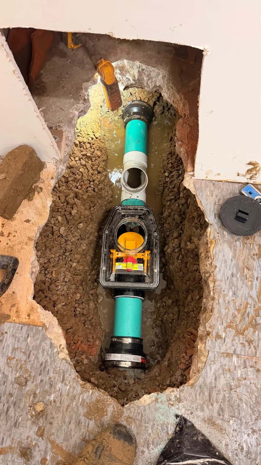 Backwater valve and pipework in an opened basement floor.